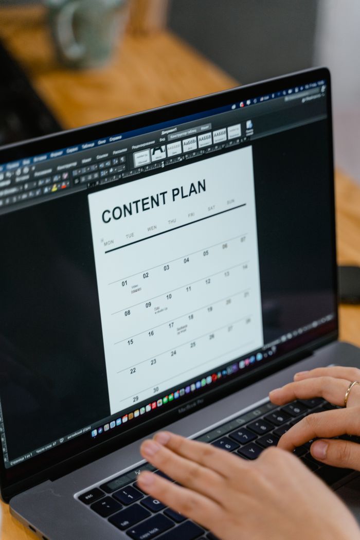 project-01-c Vue rapprochée de mains en train de taper sur un ordinateur portable affichant un document de plan de contenu, idéal pour du contenu business ou marketing.