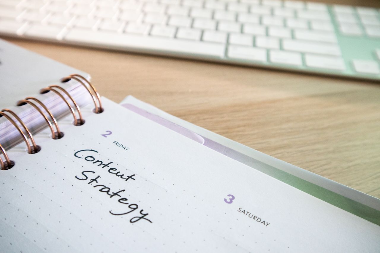 services-01 Stratégie de contenu rédigée dans un agenda, avec un clavier sur un bureau en bois